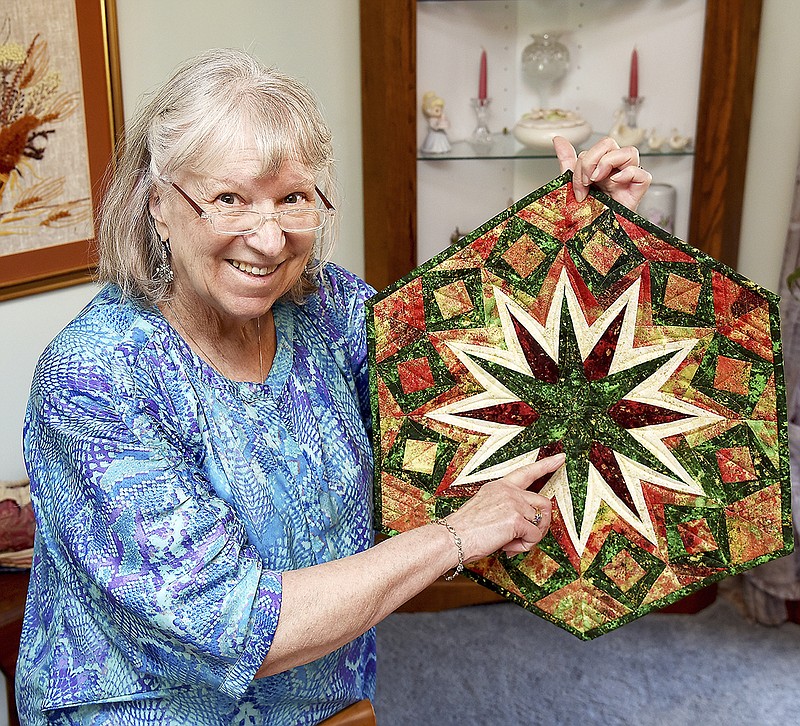 Eva Studley points to a particular stitching, above, explaining that to make the mini-quilts, the patterns on the material needs to be proportional to the size of the quilt being made. Studley tries to get people of any age involved in quilting by showing them how personalized a quilt can be, like the one she made of her cat on a stack of quilts.