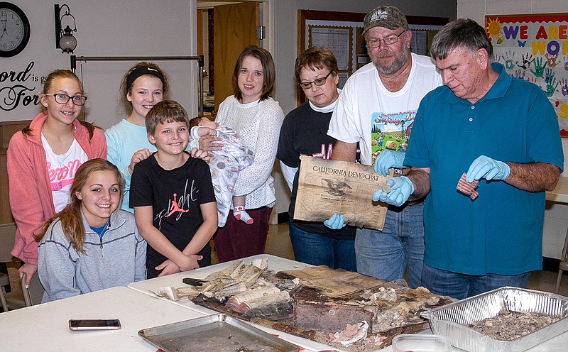 <p>Democrat photos/David A. Wilson</p><p>Checking out the contents of the recently discovered 100-year-old time capsule are, from left, Olivia Mills, Mariah Mills, Syndney Grace Pettigrew, Gabe Mills, Elise Grimes, held by her mother Lorri Longan Grimes, Devora Longan, Bruce Longan (holding a 1917 California Democrat) and Bob Staton (holding a 1917 D half dollar). Bruce is fifth generation in the church, Lorri is sixth generation and Elise is seventh generation.</p>