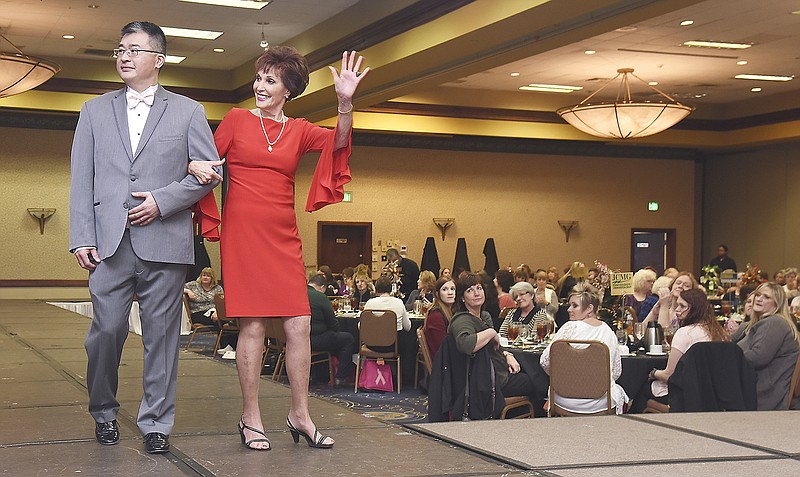 Escorted by JCMG's Dr. James Lin, three-time cancer survivor Donna Westhues waves to friends across the room as she models a red, knee-length sheath dress from Saffees during Wednesday's Strut Your Style Fashion Show and luncheon at Capitol Plaza Hotel. Proceeds from the fourth annual event will benefit The Community Breast Care Project.