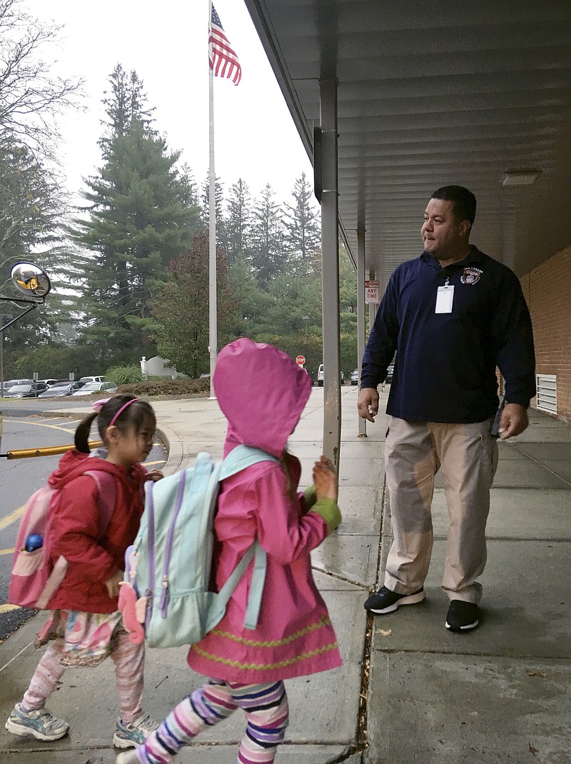 In this Nov. 6, 2017 photo, campus monitor Hector Garcia greets students as they got off the bus at the start of the school day at West Elementary School in New Canaan, Conn. Garcia and the district's other campus monitors -- all former police or corrections officers -- were among a wave of security officers hired in the aftermath of the deadly school shooting in nearby Newtown on Dec. 14, 2012. (AP Photo/Michael Melia)