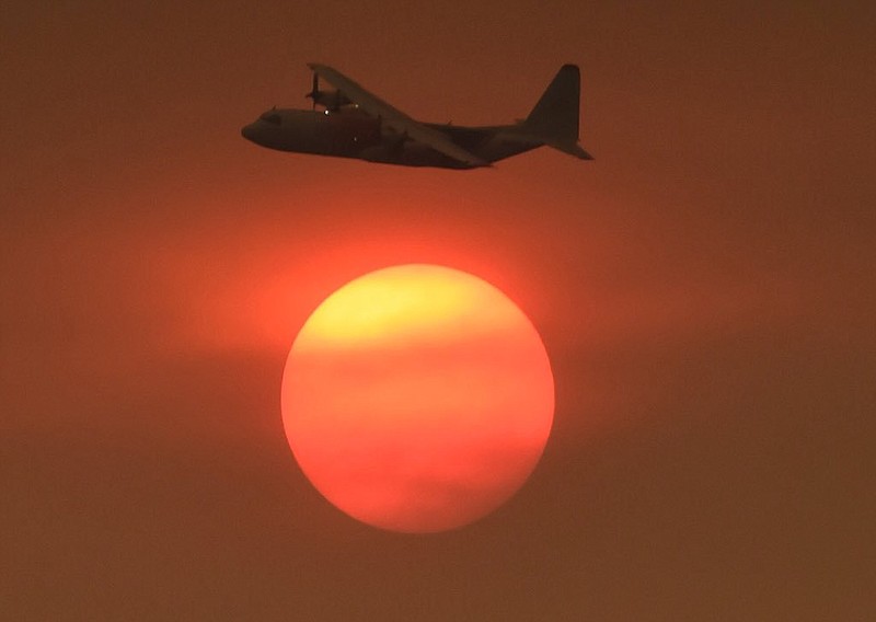 In this photo provided by the Santa Barbara County Fire Department, with smoke obscuring the sun in the distance, a Coulson C-130 Air Tanker turns in to make a drop on a hillside near Toro Canyon Road in Carpinteria, Calif., Monday, Dec. 11, 2017. Ash fell like snow and heavy smoke had residents gasping for air Monday as a wildfire exploded in size, becoming the fifth largest in state history. (Mike Eliason/Santa Barbara County Fire Department via AP)