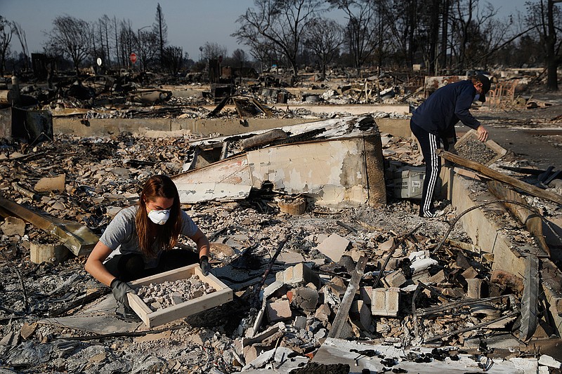 In this Oct. 15, 2017, file photo, Ed Curzon, right, and his daughter Margaret sift debris to salvage anything they can from the rubble of their home, destroyed by a wildfire in the Coffey Park neighborhood in Santa Rosa, Calif. If House Republicans have their way, victims of hurricanes in Texas and Florida could deduct their losses on their taxes. But victims of the California wildfires no longer could.