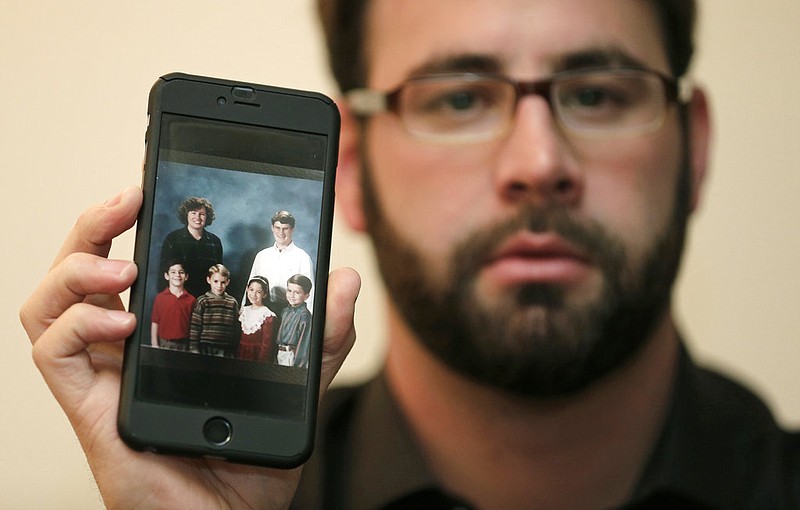 Jamey Anderson holds a photo on his phone of himself, bottom left, at the Word of Faith Christian School with classmates, from left, Liam, Risa Burgeson Pires, and Christopher Davies, and teachers Lisa Brown, top left, and Marty Roper, top right, during an interview in Charlotte, N.C., Monday, Dec. 11, 2017. Throughout his adolescence, Anderson says he was singled out as a rebel and suffered some of the most brutal treatment in the church. Among his transgressions: making a funny face at a classmate. 