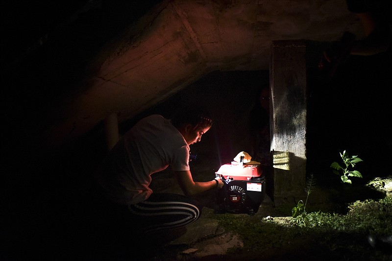 In this Dec. 21, 2017 photo, barrio Patron resident Karina Santiago Gonzalez works on a small power plant in Morovis, Puerto Rico. More than three months have passed since Hurricane Maria. Neighbors start blowing out candles and turning off generators as they go to bed around 9 p.m., having nothing else to do in the dark except sleep. (AP Photo/Carlos Giusti)