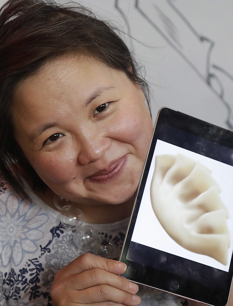 In this Wednesday, Dec. 27, 2017, photo, author Jennifer 8. Lee holds an image of a dumpling emoji while posing for photos before eating lunch at Dumpling Time restaurant in San Francisco. Thanks largely to Lee's efforts, the dumpling emoji was added to the Unicode Standard this year after almost two years of research, meetings, and a written, illustrated proposal that reads a bit like an academic paper, complete with research on dumpling history and popularity. (AP Photo/Jeff Chiu)