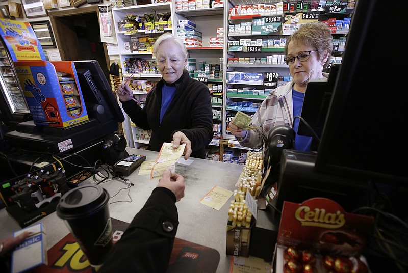 Cashiers Kathy Robinson, left, and Ethel Kroska, right, both of Merrimack, N.H., sell a lottery ticket Sunday, Jan. 7, 2018, to Diane Ackley, hand only below, at Reeds Ferry Market convenience store, in Merrimack. A lone Powerball ticket sold at Reeds Ferry Market matched all six numbers and will claim a $570 million jackpot, one day after another single ticket sold in Florida nabbed a $450 million Mega Millions grand prize. (AP Photo/Steven Senne)