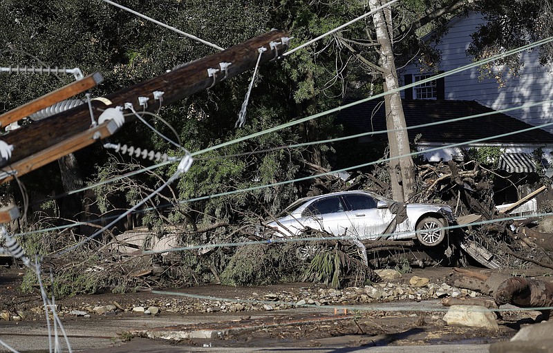 A damaged car sits over fallen and debris behind downed power lines in Montecito, Calif., Wednesday, Jan. 10, 2018. Dozens of homes were swept away or heavily damaged and several people were killed Tuesday, as downpours sent mud and boulders roaring down hills stripped of vegetation by a gigantic wildfire that raged in Southern California last month. (AP Photo/Marcio Jose Sanchez)