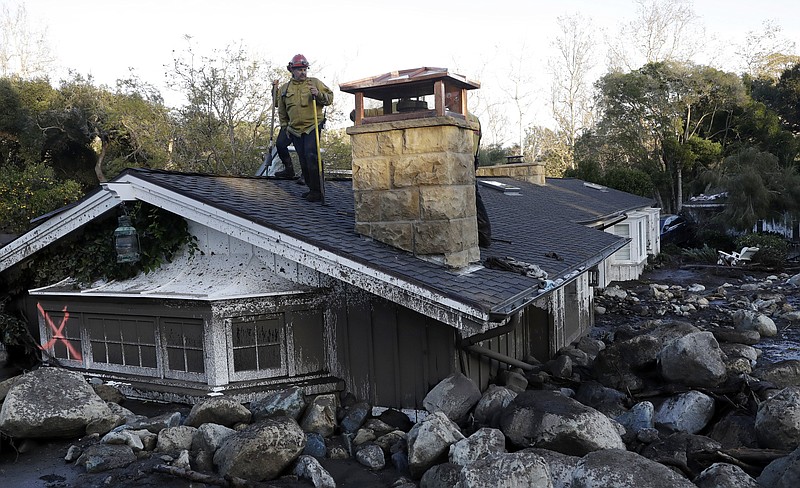 A firefighter stands on the roof of a house submerged in mud and rocks Wednesday, Jan. 10, 2018, in Montecito, Calif. Anxious family members awaited word on loved ones Wednesday as rescue crews searched grimy debris and ruins for more than a dozen people missing after mudslides in Southern California destroyed houses, swept cars to the beach and left more than a dozen victims dead. (AP Photo/Marcio Jose Sanchez)