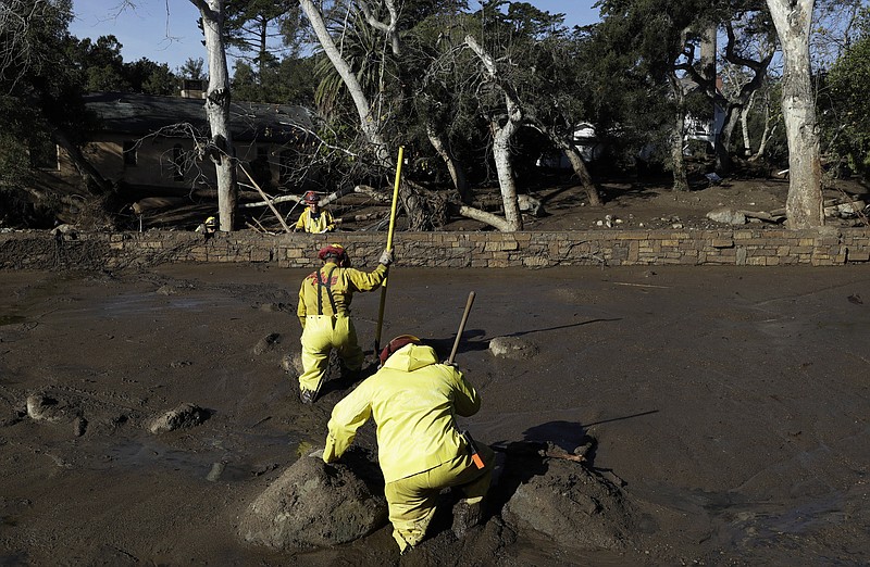 A Cal Fire search and rescue crew walks through mud near homes damaged by storms in Montecito, Calif., Friday, Jan. 12, 2018.  The mudslide, touched off by heavy rain, took many homeowners by surprise early Tuesday, despite warnings issued days in advance that mudslides were possible because recent wildfires had stripped hillsides of vegetation that normally holds soil in place.(AP Photo/Marcio Jose Sanchez)