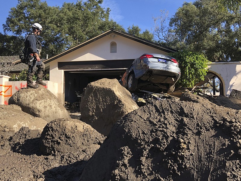 In this Saturday, Jan. 13, 2018 photo provided by the Santa Barbara County Fire Department, Capt. John Pepper, Fresno Fire Department, and Rescue Squad Leader RTF-5 searches homes off East Valley Road in Montecito, Calif. (Mike Eliason/Santa Barbara County Fire Department via AP)