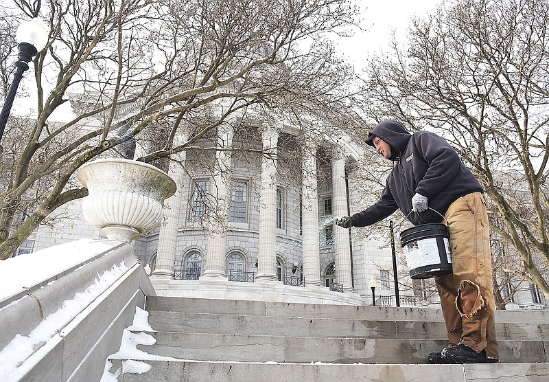 Dressed in heavy winter wear, Payton Turpin scatters ice-melting material on the steps of the north side of the Capitol on Monday, Jan. 15, 2018. Facilities management crews were busy clearing walkways and steps of snow before employees return to work Tuesday. Foot and street traffic was minimal due to the Martin Luther King Jr. state holiday.