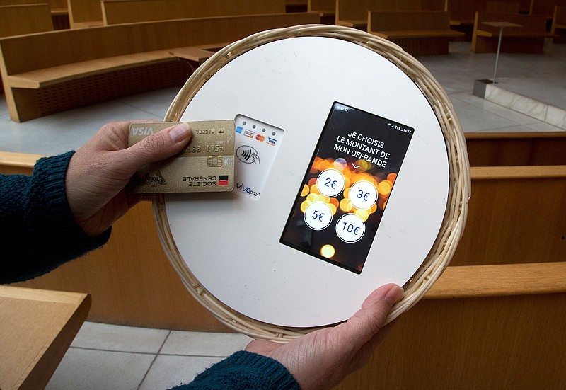 Father Didier Duverne demonstrates how works the contactless card payments device in a collection basket at the Saint Francois de Molitor church in Paris, Thursday, Jan.18, 2018. The city's diocese will introduce the system during Sunday's mass. Mass attenders will choose on a screen the amount they want to donate — from 2 to 10 euros ($2.4 to $12.2) — and their payment will be processed in "one second." (AP Photo/Michel Euler)