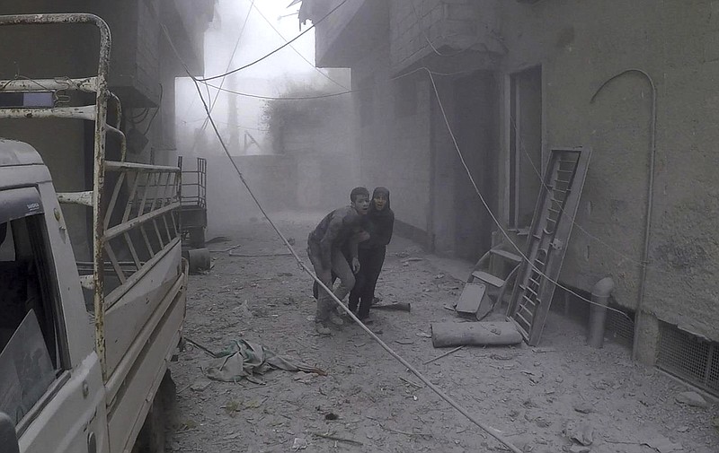 This photo provided by the Syrian Civil Defense group known as the White Helmets, shows two civilians fleeing from the scene of an attack after airstrikes hit a rebel-held suburb near Damascus, Syria, Monday, Feb. 5, 2018. Syrian opposition activists said more than one dozen people killed in new airstrikes. (Syrian Civil Defense White Helmets via AP)