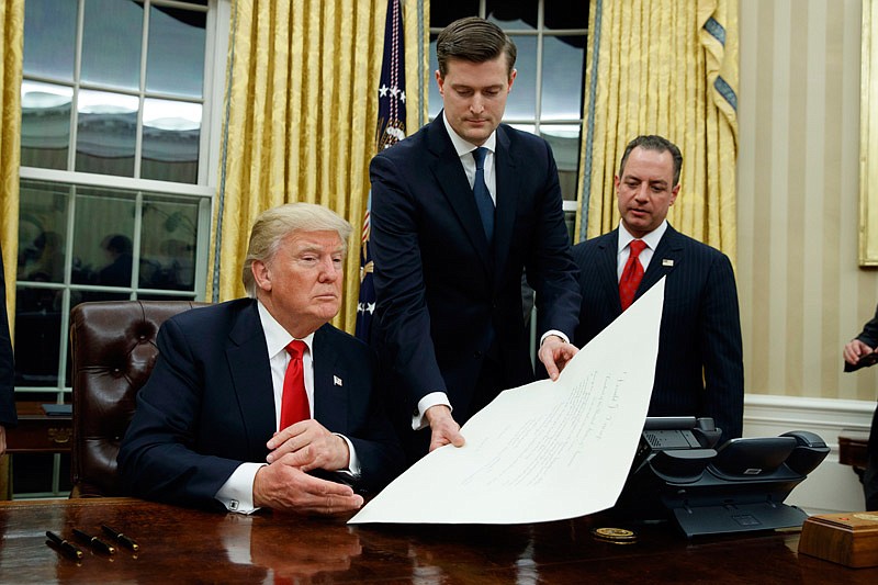 In this Jan. 20, 2017 file photo, White House Staff Secretary Rob Porter, center, hands President Donald Trump a confirmation order for James Mattis as defense secretary, in the Oval Office of the White House in Washington, as White House Chief of Staff Reince Priebus, right, watches.  Porter is stepping down following allegations of domestic abuse by his two ex-wives.   (AP Photo/Evan Vucci)