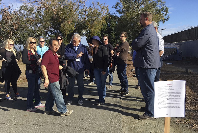 Judge David Carter, a U.S. District Judge, sixth from left, pointing, followed by an entourage of three dozen lawyers, Orange County workers, nonprofit staff and local officials tours a Southern California homeless encampment amid a lawsuit over efforts by local officials to shut it down in Santa Ana, Calif., Wednesday, Feb. 14, 2018. Judge Carter is overseeing a lawsuit filed by homeless advocates over the planned closure of the encampment on the county-owned trail. (AP Photo/Amy Taxin)