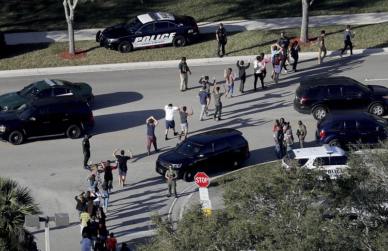 FILE - In this Feb. 14, 2018 file photo,  students hold their hands in the air as they are evacuated by police from Marjory Stoneman Douglas High School in Parkland, Fla., after a shooter opened fire on the campus.  Students are taught to evacuate during fire alarms but lock down during school shootings. So there was confusion Wednesday when a fire alarm sounded,  the second one that day at the high school as 19-year-old former student Nikolas Cruz unleashed a barrage of gunfire. Head for the exits or hunker down in classrooms? (Mike Stocker/South Florida Sun-Sentinel via AP, File)