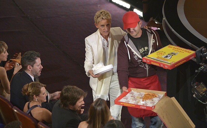 In this March 2, 2014 file photo, host Ellen DeGeneres passes out pizza in the audience during the Oscars in Los Angeles. DeGeneres, who also hosted in 2007, started a trend during the 2014 show by feeding the actors with a surprise pizza deliveryand taking up a collection to pay the pizza guy. (Photo by John Shearer/Invision/AP, File)