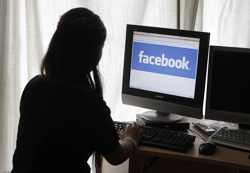 FILE - In this June 4, 2012 file photo, a girl looks at Facebook on her computer in Palo Alto, Calif. Baffled in 2016 by Russian agents who bought ads in an attempt to sway the U.S. presidential campaign, Facebook told the National Association of Secretaries of State on Saturday, Feb. 17, 2018, that the company would send postcards to potential buyers of political ads to confirm they reside in the U.S. The plan was unveiled a day after special counsel Robert Mueller charged 13 Russians with interfering in the presidential election. (AP Photo/Paul Sakuma, File)