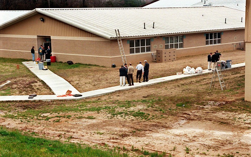 In this March 24, 1998 file photo, officials examine the scene at Westside Middle School in Jonesboro, Ark. after two boys fired on teachers and students.  The two boys with stolen guns took aim from a wooded hill, waiting for people to evacuate after one of the boys had triggered a false fire alarm. They killed four children and a teacher. That was 20 years ago, today students are taught to evacuate during fire alarms but lock down during school shootings. So there was confusion Wednesday, Feb. 14, 2018 when a fire alarm sounded, the second one that day, at a Florida high school as former student Nikolas Cruz unleashed a barrage of gunfire. Head for the exits or hunker down in classrooms?   (Leigh Daughtridge/The Commercial Appeal via AP)