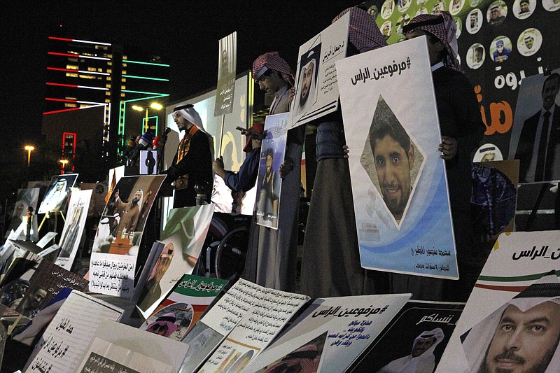 In this Feb. 14, 2018 photo, opposition activist and former lawmaker Bader al-Dahoum speaks during a protest near Kuwait's parliament in Kuwait City, Kuwait. A pending court case in Kuwait against dozens of politicians, activists and others stemming from the country’s 2011 Arab Spring protests represents a rare crackdown on dissent in what is relatively the most politically open country among the Gulf Arab states. The posters displayed show some of those detained with the hashtag in Arabic reading, "With Heads Held High." (AP Photo/Jon Gambrell)