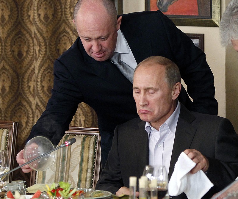 FILE - In this Friday, Nov. 11, 2011, file photo, Yevgeny Prigozhin, left, serves food to Russian Prime Minister Vladimir Putin during dinner at Prigozhin's restaurant outside Moscow, Russia. Progozhin is known as “Putin’s chef” _ a wealthy Russian businessman and restaurateur who gained favor with Putin through his stomach. On Feb. 16, 2016, Prigozhin, along with 12 other Russians and three Russian organizations, was charged by the U.S. government as part of a vast and wide-ranging effort to sway political opinion during the 2016 U.S. presidential election. According to the indictment, Prigozhin and his companies provided significant funding to the Internet Research Agency, a St. Petersburg-based troll farm that allegedly used bogus social media postings and advertisements fraudulently purchased in the name of Americans to influence the White House race. (AP Photo/Misha Japaridze, Pool, File)