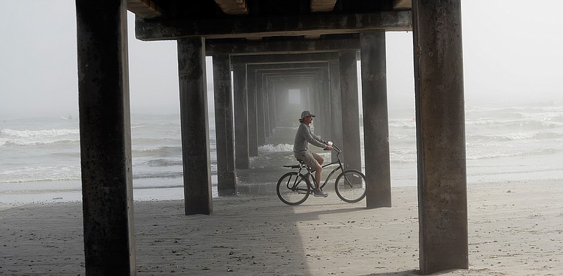 A cyclist passes a pier on the beach as a heavy fog moves into the area Saturday in Port Aransas, Texas.
