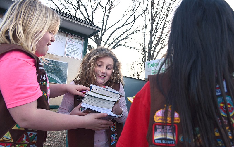 Elle Newman, 9, center, receives books from Madison Smith, 9, to put them in the new "Little Free Library" on Monday at Cole County Park. The new book exchange has multiple shelves and can hold almost twice as many books as the original book exchange. Vandals burned the previous library down in January, but that didn't stop community members from coming together to rebuild.