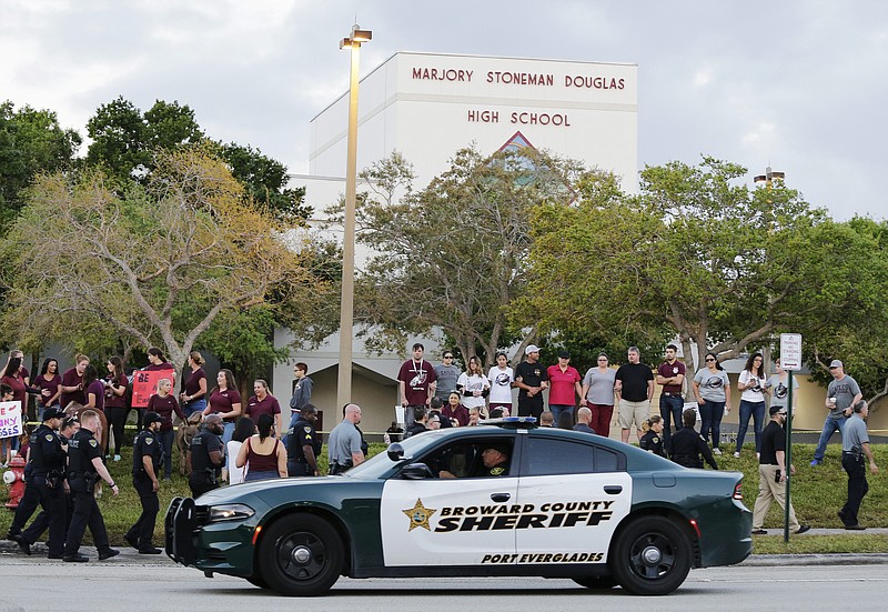 In this Feb. 28, 2018 photo, a police car drives by Marjory Stoneman Douglas High School in Parkland, Fla., as students returned to class for the first time since a former student opened fire there with an assault weapon. The United States is in the midst of a national debate over school security after the mass shooting at a Florida school. To President Donald Trump and gun supporters, the solution is to put more guns in the hands of trained school staff _ including teachers _ to “play defense” against a rampaging gunman. The rest of the world has different strategies to deal with violence around schools. But the U.S. appears to be the only place in the world that wants to arm teachers to the degree the president wants.   (AP Photo/Terry Renna)