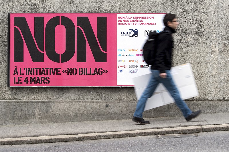 FILE - In this Feb. 9, 2018 photo a man passes by a sign asking to vote in the "No Billag" initiative in Fribourg, Switzerland. Swiss voters can decide in a referendum on March 4, 2018 on a proposal to stop the mandatory licence fee for services of the Swiss Broadcasting Corporation.  (Anthony Anex/Keystone via AP)