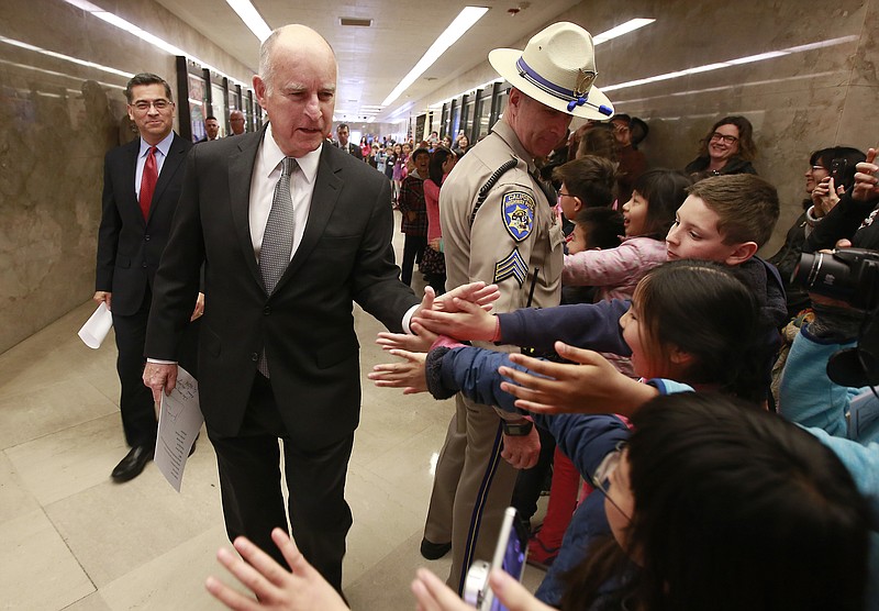 California Gov. Jerry Brown is greeted by children as he walks through the Capitol with California Attorney General Xavier Becerra, left, to hold a news conference in response to remarks made U.S. Attorney General Jeff Sessions, Wednesday, March 7, 2018, in Sacramento, Calif. (AP Photo/Rich Pedroncelli)