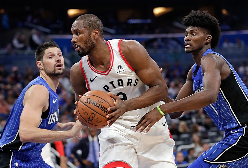 Toronto Raptors' Serge Ibaka, center, looks for a way to the basket as he gets between Orlando Magic's Nikola Vucevic, left, and Jonathan Isaac, right, during the first half of an NBA basketball game, Tuesday, March 20, 2018, in Orlando, Fla. (AP Photo/John Raoux)