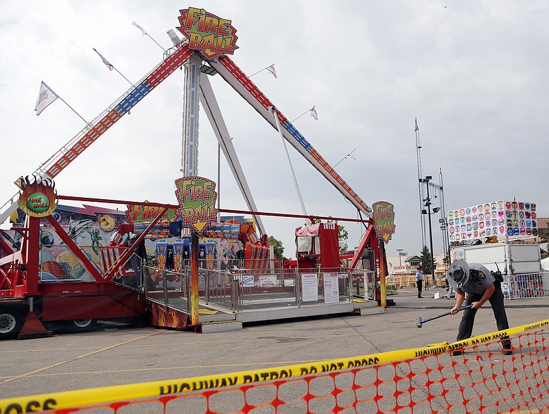 FILE - In this July 27, 2017 file photo, an Ohio State Highway Patrol trooper removes a ground spike in front of the Fire Ball ride at the Ohio State Fair, in Columbus, Ohio. Attorneys for the family of a teenager killed in a thrill ride accident at the Ohio State Fair and others left with life-changing injuries believe the state's inspectors missed obvious warning signs. But the attorneys won't include the state in any lawsuits or financial settlements because Ohio, like many other states, gives its carnival ride inspectors immunity from accusations of negligence. (AP Photo/Jay LaPrete, File)
