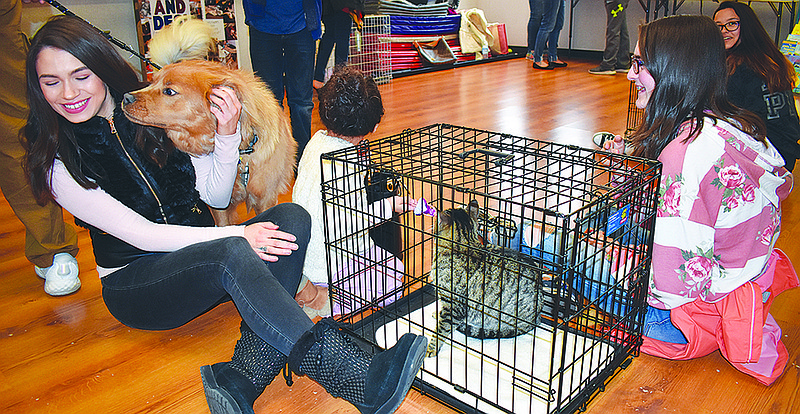 Jefferson City resident Maja Kadic gets attention from a dog while visiting a cat during Sunday's People Helping Paws "Kitten Shower" event. To the right of her are Leyla Kadic, 4, and Emma Smith, 14, of Ashland.