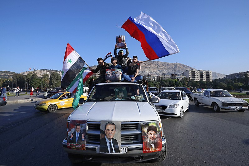 Syrian government supporters wave Syrian, Iranian and Russian flags as they chant slogans against U.S. President Trump during demonstrations following a wave of U.S., British and French military strikes to punish President Bashar Assad for suspected chemical attack against civilians, in Damascus, Syria, Saturday, April 14, 2018. Hundreds of Syrians are demonstrating in a landmark square in the Syrian capital, waving victory signs and honking their car horns in a show of defiance. (AP Photo/Hassan Ammar)