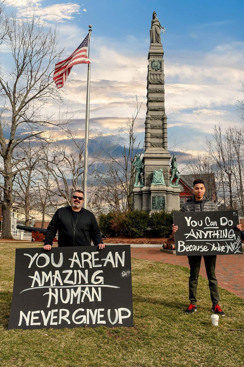In this April 8, 2018 photo, Greg Amaral, left, and Wendell Walker, right, stand with signs showing positive messages in front of the Soldiers and Sailors Monument on Main Street, in Nashua, N.H.  The two have showed up on with feel-good signs each weekend since Easter Sunday. They say their goal is to encourage people to be happy and follow their dreams. (Craig Michaud via AP)