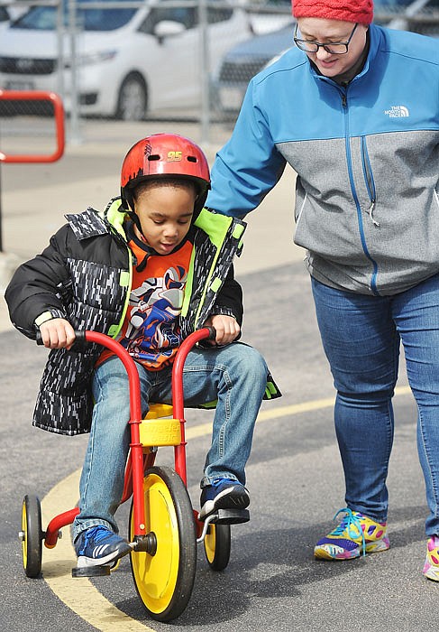 Scholastic volunteer Crystal Perkins assists Solomon Wilkerson on Thursday as he rides his tricycle around the playground at Southwest Early Childhood Center as the school celebrated Week of the Young Child with a field day at the school. 