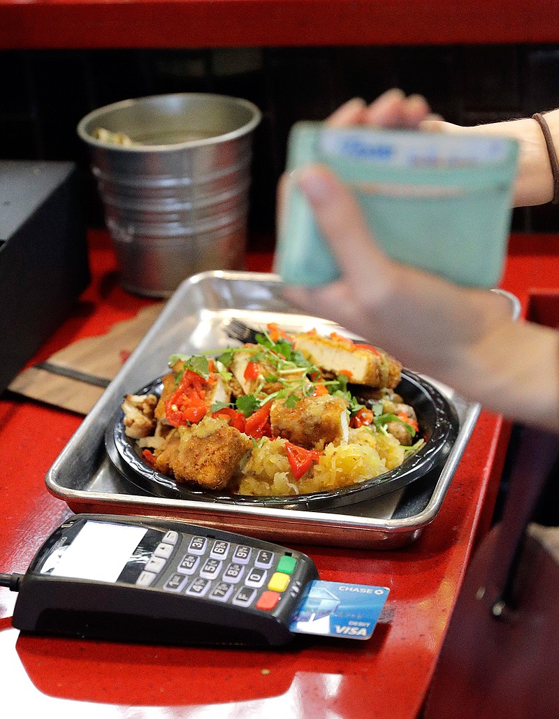 In this Tuesday, April 10, 2018, photo, a customers uses a credit card machine to pay for food at Peli Peli Kitchen in Houston. Owner Thomas Nguyen had a change of heart after transitioning one of his three Peli Peli South African fine dining restaurants and his Peli Peli Kitchen fast casual location to a no-cash policy. (AP Photo/David J. Phillip)