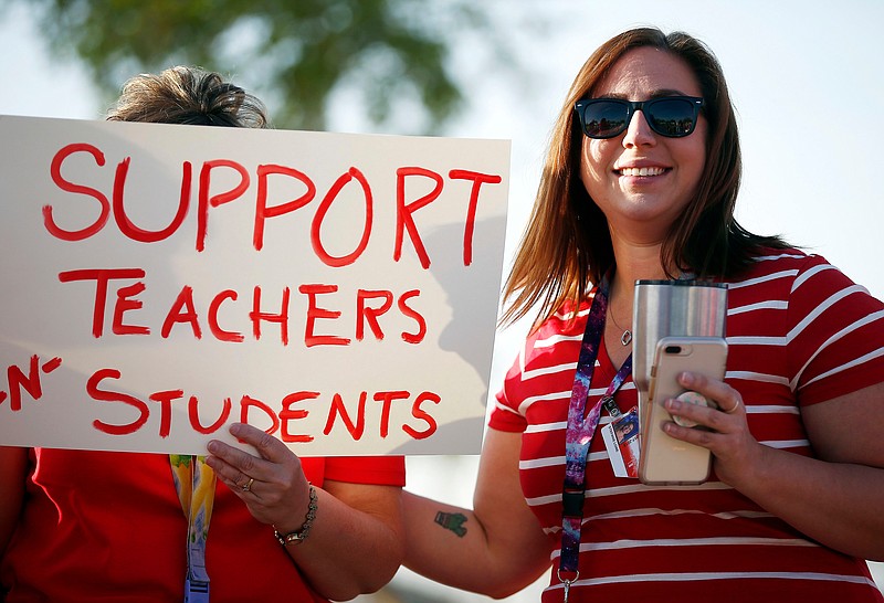 FILE - In this April 11, 2018, file photo, Stefanie Lowe, a teacher at Tuscano Elementary School, smiles as she joins other teachers, parents and students as they stage a "walk-in" for higher pay and school funding in Phoenix. Tens of thousands of Arizona teachers are poised to participate in a statewide job action this week in an unprecedented walkout to demand more funding for public education. (AP Photo/Ross D. Franklin, File)