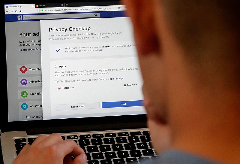 FILE - In this March 26, 2018, file photo, a man poses for photos in front of a computer showing Facebook.