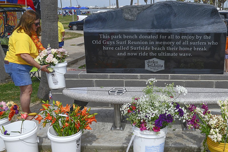 In a Saturday, April 28, 2018 photo, Alice Castle puts flowers next to the new monument dedicated by the Old Guys Surf Reunion in Surfside Beach, Texas. It took five years to raise the money for the monument. 