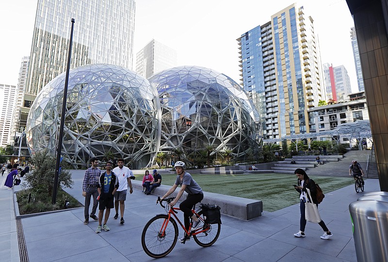In this Monday, May 7, 2018, photo, pedestrians and cyclists gather near the Amazon Spheres, in Seattle. Seattle's latest tax proposal to combat homelessness takes aim at large businesses such as Amazon that have helped drive the city's economic boom. But businesses and others say the so-called head tax is misguided and potentially harmful and they question whether the city is effectively using the tens of millions of dollars it already spends on homelessness each year. (AP Photo/Ted S. Warren)