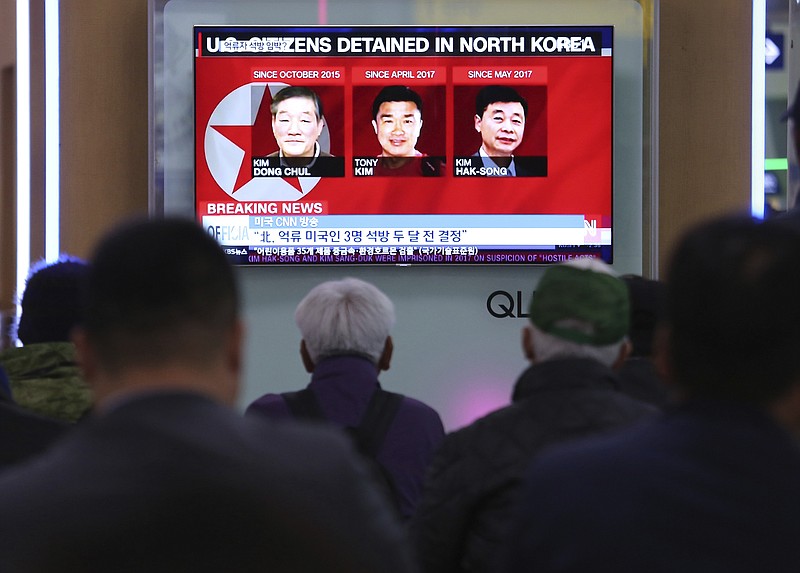 In this May 3, 2018 photo, people watch a TV news report screen showing portraits of three Americans, Kim Dong Chul, left, Tony Kim and Kim Hak Song, right, detained in the North Korea, at the Seoul Railway Station in Seoul, South Korea   President Donald Trump says Secretary of State Mike Pompeo is on his way back from North Korea with three American detainees, saying they "seem to be in good health."  (AP Photo/Ahn Young-joon)