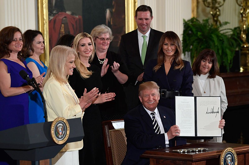 President Donald Trump holds up an executive order he signed as he is surrounded by first lady Melania Trump, second from right, Karen Pence, right, White House counselor Kellyanne Conway, third from left, Ivanka Trump, fourth from left, and others during a celebration of military mothers and spouses event in the East Room of the White House in Washington, Wednesday, May 9, 2018. The executive order addressed military spouse unemployment by providing greater opportunity for military spouses to be considered for federal competitive service positions, and holding agencies accountable for increasing their use of the non-competitive hiring authority for military spouses.  (AP Photo/Susan Walsh)