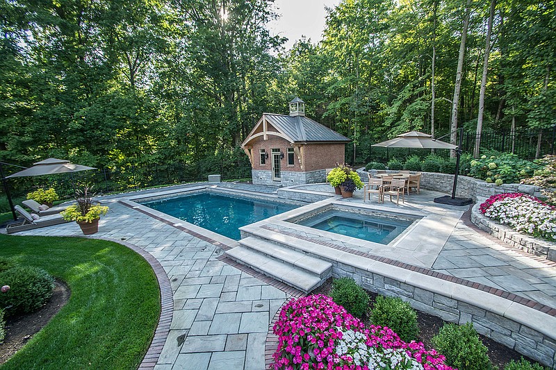 This 2017 photo provided by Grunder Landscaping shows a contrasting mix of long-flowering plants separated from the pool water by a walkway in Dayton, Ohio. Poolside landscaping is a bit more demanding than the usual. Container plants can be moved to follow the sun while trees are kept well in the background to help prevent leaf litter. (Peter Winburg/Grunder Landscaping via AP)