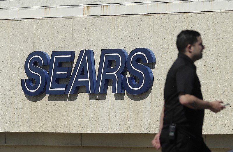 FILE- In this March 28, 2018, file photo, a man walks in front of a Sears sign in San Bruno, Calif. In a move announced Monday, May 14, Sears Holdings Corp. says a special committee of its board is starting a formal process to explore the sale of its Kenmore brand and related assets. (AP Photo/Jeff Chiu, File)