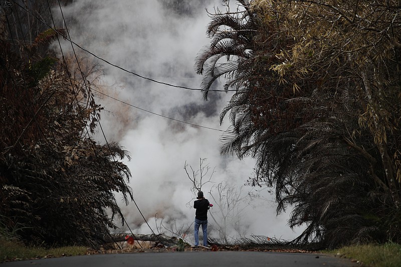 A resident photographs toxic gases emitting from cracks in the Leilani Estates subdivision near Pahoa, Hawaii Saturday, May 19, 2018. Two fissures that opened up in a rural Hawaii community have merged to produce faster and more fluid lava. Scientists say the characteristics of lava oozing from fissures in the ground has changed significantly as new magma mixes with decades-old stored lava.(AP Photo/Jae C. Hong)