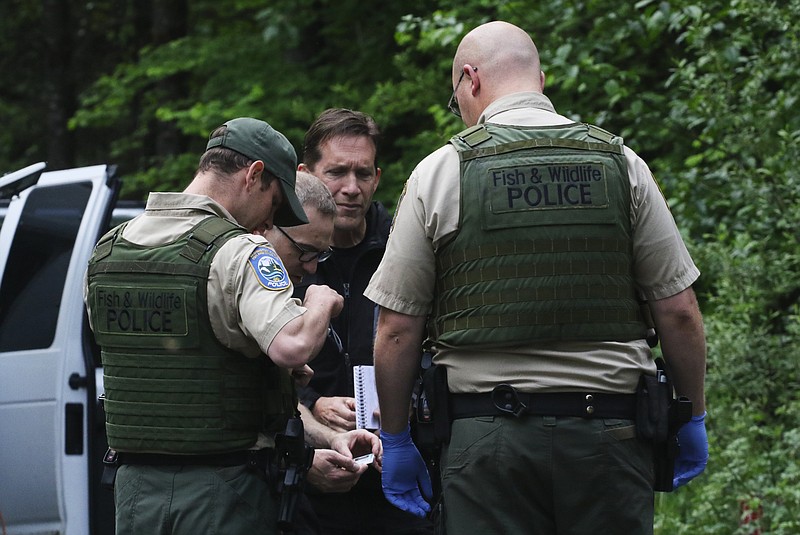 Washington State Fish and Wildlife Police confer with an individual from the King County Medical Examiner's and a King County Sheriff's deputy on a remote gravel road above Snoqualmie, WA., following a fatal cougar attack. Saturday May 19, 2018. One man was killed and another seriously injured when they encountered a cougar Saturday while mountain biking in Washington state, officials said. (Alan Berner /The Seattle Times via AP)