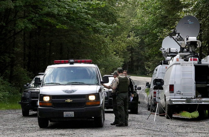 Washington State Fish and Wildlife Police confer with an individual from the King County Medical Examiner's office on a remote gravel road above Snoqualmie, Wash., following a fatal cougar attack, Saturday, May 19, 2018.  One man was killed and another seriously injured when they encountered a cougar Saturday while mountain biking in Washington state, officials said. (Alan Berner/The Seattle Times via AP)