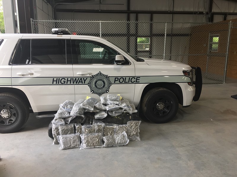 Bundles of marijuana are piled near an Arkansas Highway Police vehicle after officers found the drugs on a transporter carrying a load of cars on Interstate 40 near Van Buren. Three people were arrested, and $7,160 in cash was seized. (Photo courtesy of Arkansas Department of Transportation)