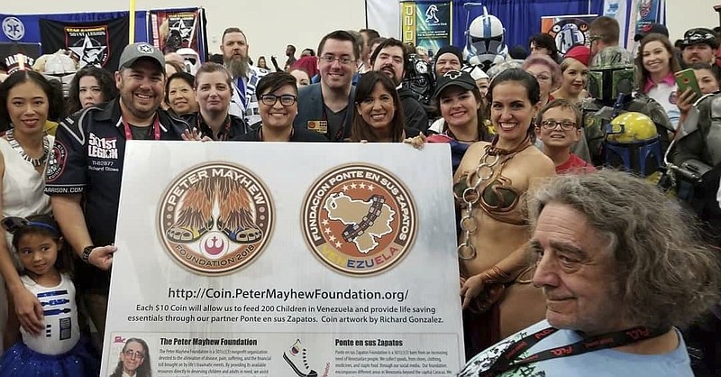 This May 29, 2018 photo provided by Elisa Arguello shows actor Peter Mayhew, front right, posing for a photo with members of the "Star Garrison," the Texas chapter of Star Wars Fan Club "501st Legion," including Venezuelan Elisa Arguello, dressed as Princes Leia, as they launch the Chewbacca Challenge Coin, a fundraising campaign whose proceeds will benefit a charity feeding underprivileged children in Venezuela, during the Comicpalooza event in Houston Texas. The copper coins are being sold online for $10 by the Peter Mayhew foundation. But proceeds will go to “Ponte en sus zapatos, a small Texas charity that has been working in Venezuela for over a year and claims to feed 100 needy children every day. (Elisa Arguello via AP)